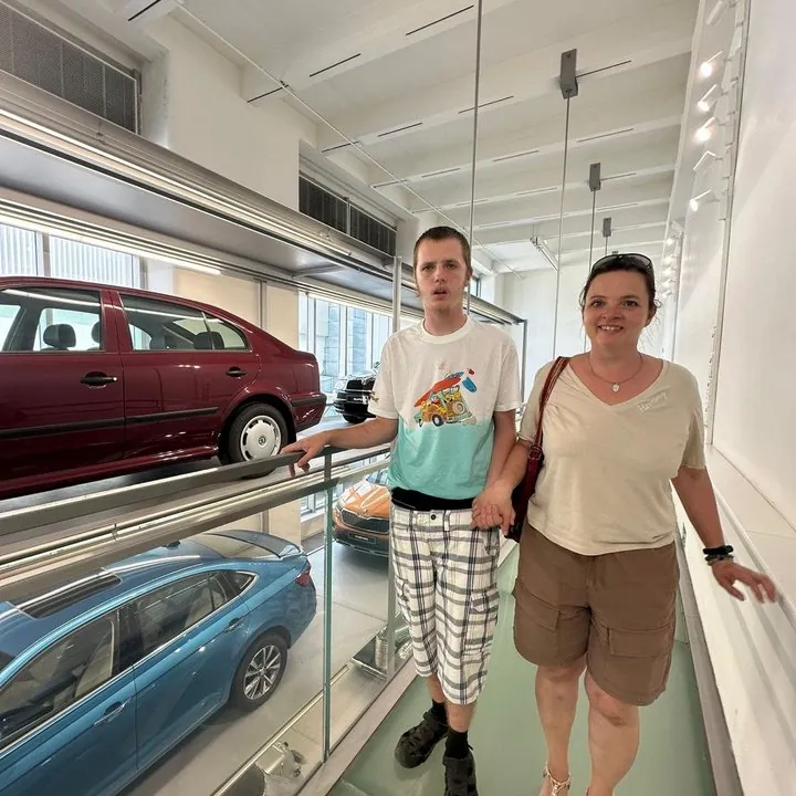 Mężczyzna i jego mama trzymają się za rękę na szklanym moście w muzeum z samochodami